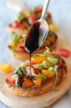 Vegetarian Avocado Bruschetta with Balsamic Reduction | This bruschetta recipe brightens up the smooth texture of ripe avocado with the juicy tartness of grape tomatoes. Serve it with a spoonful of balsamic reduction to complete the midday treat or party snack! //