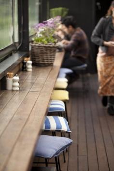 the idea of using small bright/cool/patterned cushions on barstools to brighten up/add interest to bar space in a cafe like this