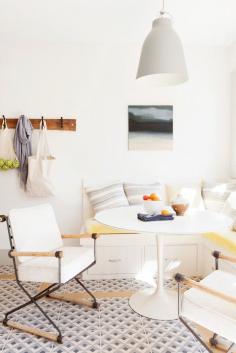 
                    
                        Bright white kitchen nook featuring yellow bench seating, patterned tile floors, and industrial steel and wood armchairs.
                    
                